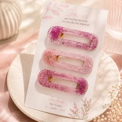 Tres ganchos para el cabello en resina rosada con flores naturales y glitter, en una tarjeta impresa de agradecimiento
