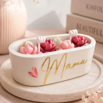 Jardinera ovalada de cera con flores modeladas en tonos rosados y la palabra Mama en vinilo dorado