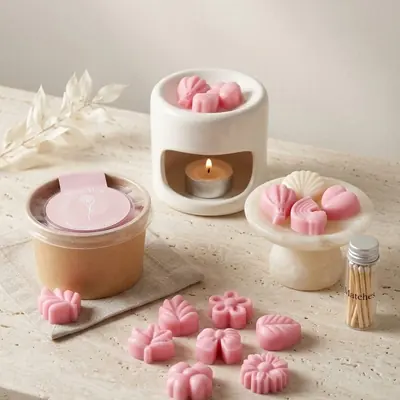 Pebetero de cerámica encendido con wax melts, potecito con figuras de cera, y frasco de fósforos