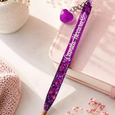 Lapicero forrado en resina con glitter morado, el nombre completo en vinilo blanco y un dije de corazón