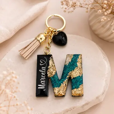 Llavero de resina con la letra M en negro, glitter esmeralda y hoja de oro, nombre en blanco y borla beige