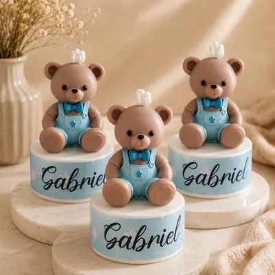 Velas con forma de osito con overol azul y corbatín, sobre base y el nombre Gabriel