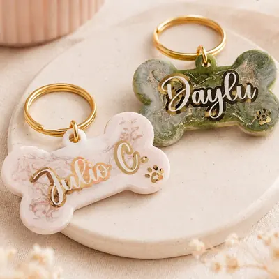 Dos placas de resina con forma de hueso, en verde y rosado marmoleado con hoja de oro, con el nombre de la mascota