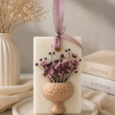 Sachet de cera aromática color marfil con florero en relieve, flores secas moradas y cinta de organza