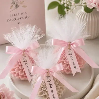 Tres velas con forma de dalia envueltas en tul blanco con lazo rosa y tarjeta Feliz día mamá