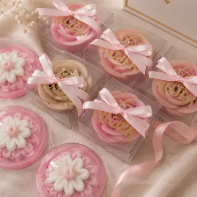 Velas con forma de rosa y margarita rosadas con lazo de satín, en cajas transparentes de la Colección Especial