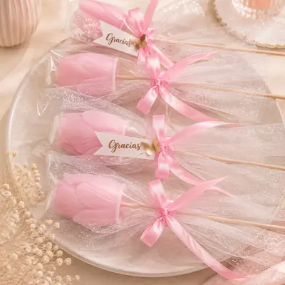 Velas con forma de tulipán rosado envueltas en tul con brillo, lazo rosado y etiqueta de gracias