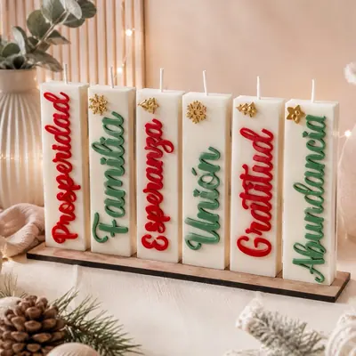 Seis velas rectangulares blancas con palabras en rojo y verde y apliques dorados de copo de nieve y estrella